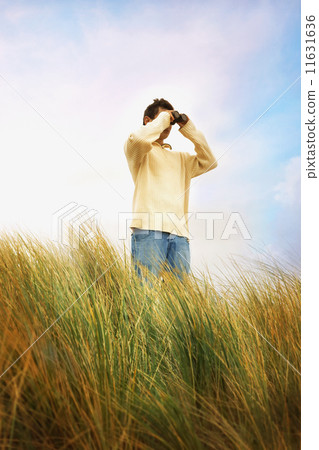 Man standing in dune grass using binoculars 11631636
