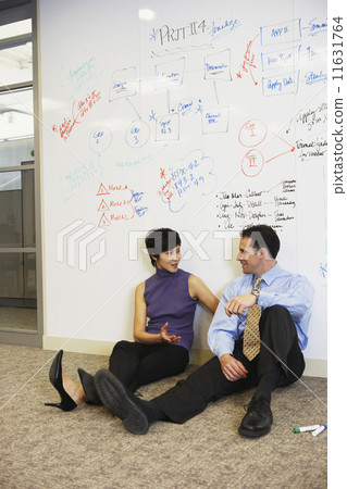 Two businesspeople sitting on floor in front of whiteboard wall 11631764