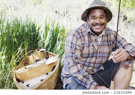 Middle aged African man with fishing gear next to canoe 11631899
