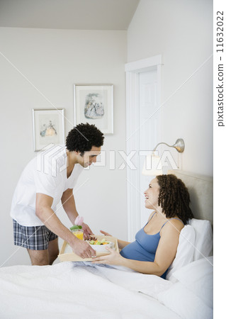 Pregnant African woman getting breakfast in bed 11632022