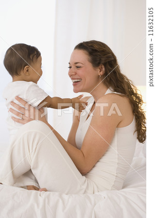 Hispanic mother playing with baby on bed Hispanic mother playing with baby on bed 11632105
