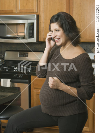 Pregnant Hispanic woman talking on telephone 11632202