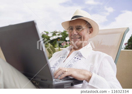 Senior man typing on laptop in lounge chair 11632334