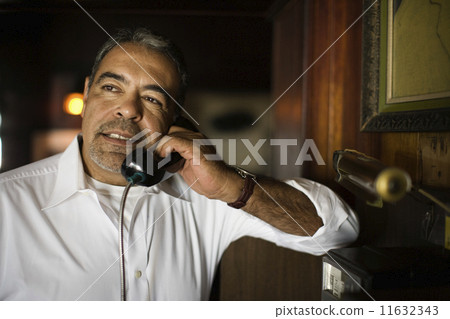 Hispanic man talking on pay telephone Hispanic man talking on pay telephone 11632343