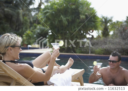 Couple having cocktails at swimming pool 11632513