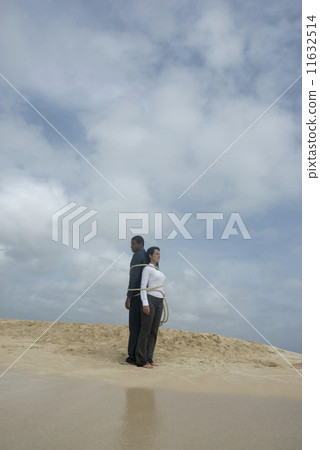 Multi-ethnic businesspeople tied together at beach Multi-ethnic businesspeople tied together at beach 11632514