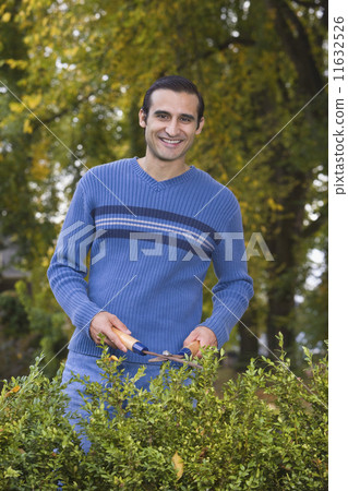 Hispanic man trimming hedges 11632526
