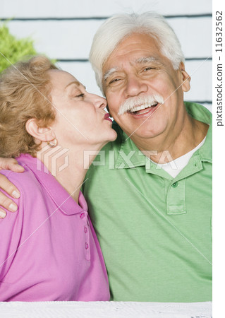 Senior Hispanic woman kissing husband's cheek 11632562