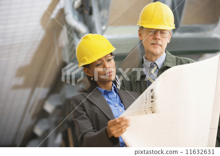 Two businesspeople in hard hats looking at blueprints Two businesspeople in hard hats looking at blueprints 11632631