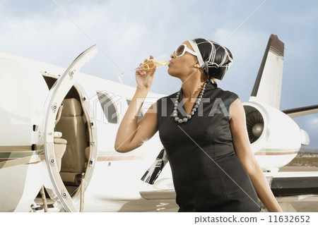 African American woman drinking champagne next to airplane 11632652