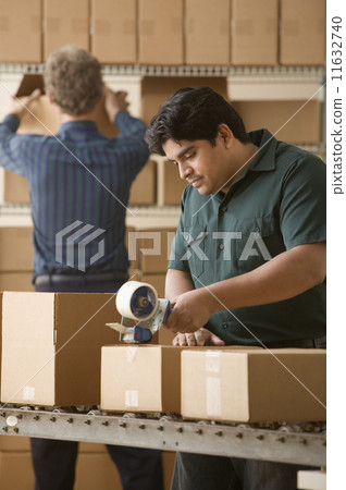 Young man taping a cardboard box closed Young man taping a cardboard box closed 11632740