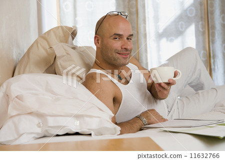 Hispanic man holding coffee mug in bed 11632766