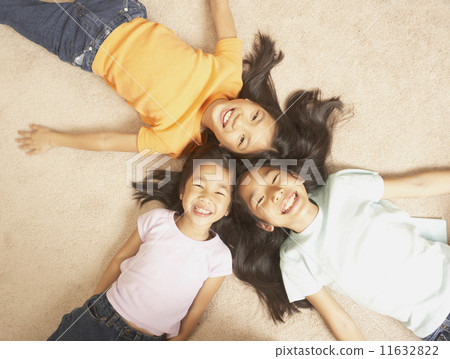 Three young Asian sisters lying on the floor with their heads together  11632822