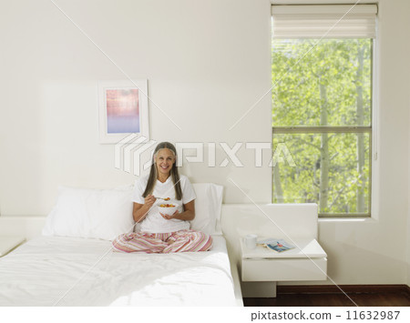 Asian woman eating cereal in bed 11632987