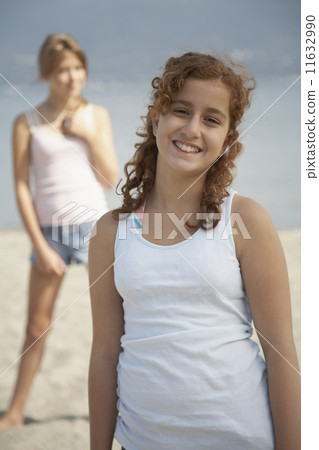 Teenage girl smiling on beach with friend in background 11632990