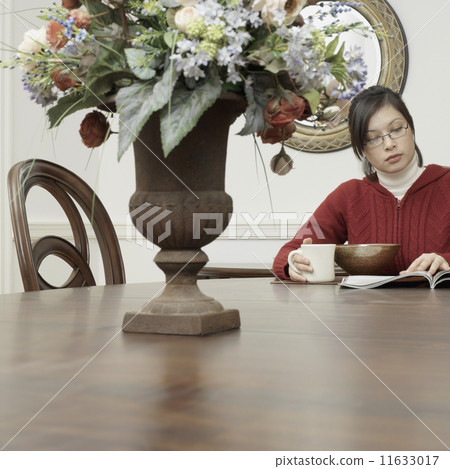 Asian woman eating and reading at dining table 11633017