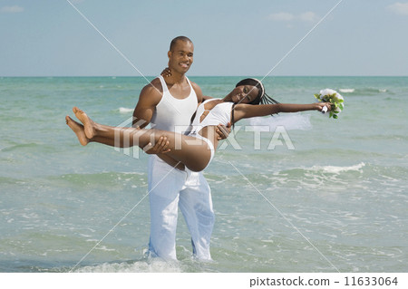 African groom carrying bride at beach 11633064