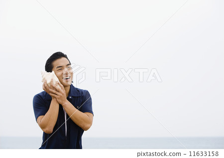 Asian man listening to conch shell 11633158