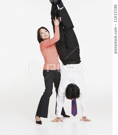 Studio shot of Asian businessman doing handstand with Asian businesswoman's help 11633186