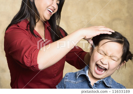 Asian mother fixing yelling daughter's hair 11633189