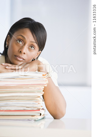 African American businesswoman leaning on stack of paperwork African American businesswoman leaning on stack of paperwork 11633316