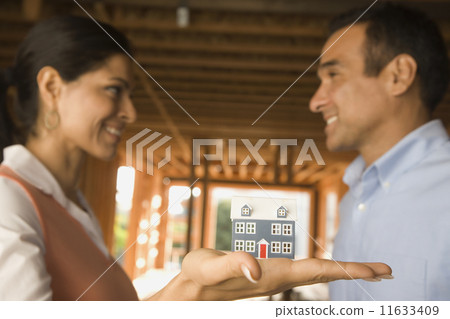 Hispanic couple holding model house at construction site 11633409