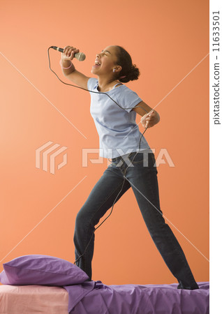 Girl singing with microphone standing on bed Girl singing with microphone standing on bed 11633501