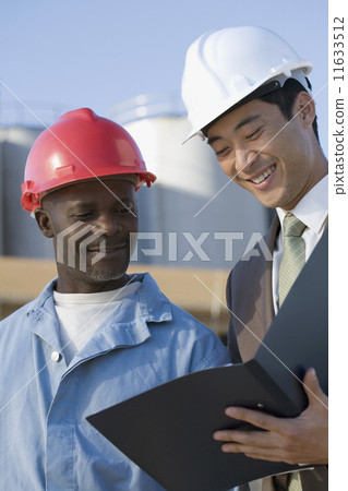 Multi-ethnic businessman and construction worker looking at paperwork Multi-ethnic businessman and construction worker looking at paperwork 11633512