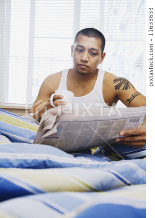 Asian man reading newspaper in bed 11633633