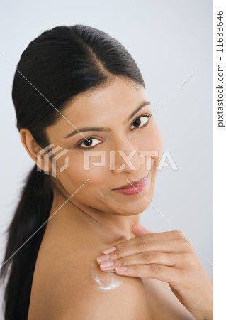 Indian woman applying lotion to shoulder 11633646