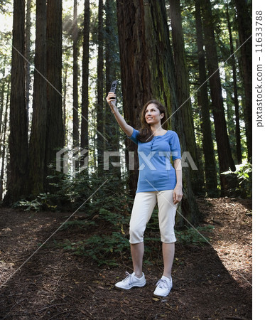 Hispanic woman taking photograph in woods 11633788
