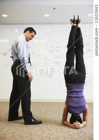 Businesswoman doing headstand next to businessman in front of whiteboard wall Businesswoman doing headstand next to businessman in front of whiteboard wall 11633843