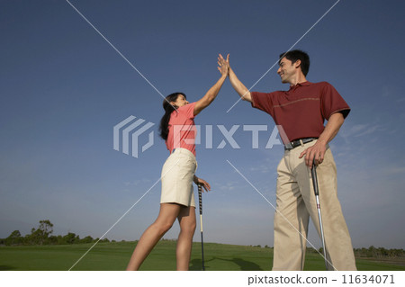 Hispanic couple high-fiving on golf course 11634071