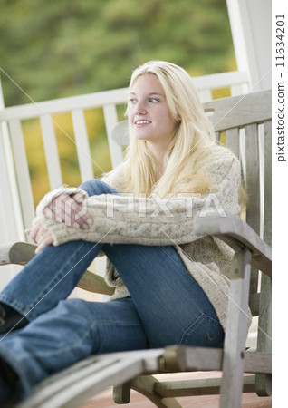 Young woman in sweater sitting on porch 11634201