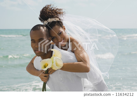 Multi-ethnic bride and groom hugging at beach 11634212