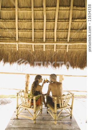 Couple drinking beer at a table underneath thatch roof 11634338