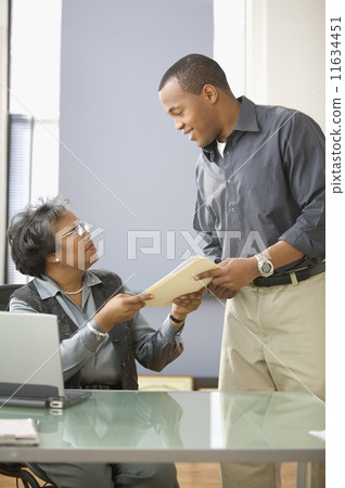 Mature woman handing man file in office 11634451