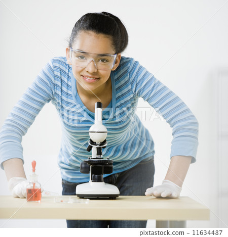 Mixed Race teenage girl using microscope 11634487