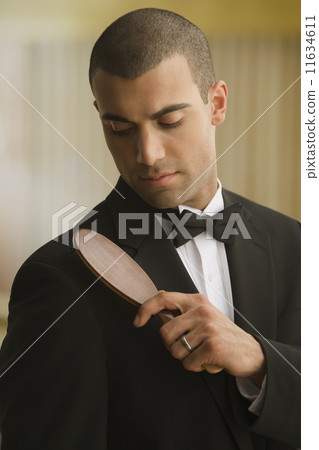 Hispanic man brushing lint off tuxedo 11634611