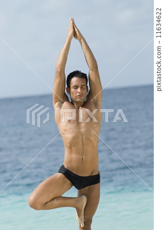 Hispanic man practicing yoga at beach 11634622