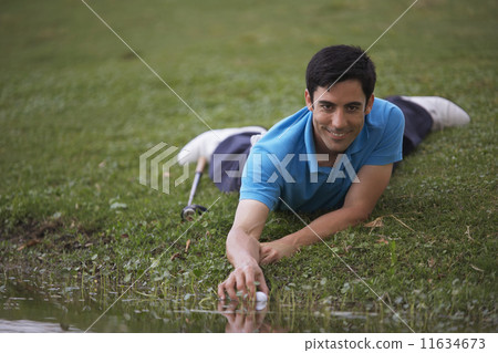 Hispanic man reaching for golf ball in water 11634673