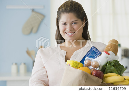 Hispanic woman holding bag of groceries 11634709