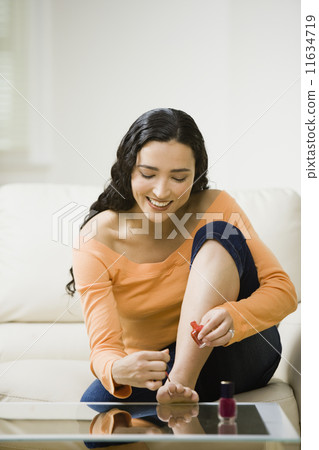 Hispanic woman painting toenails 11634719
