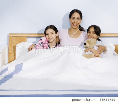 Hispanic mother and daughters sitting in bed Hispanic mother and daughters sitting in bed 11634735