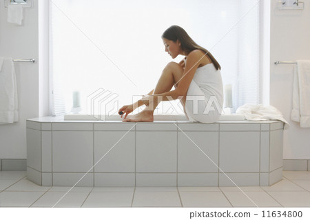 Woman wrapped in towel painting toenails on side of tub Woman wrapped in towel painting toenails on side of tub 11634800