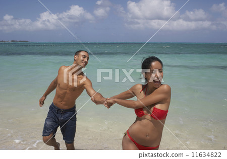 Hispanic woman pulling boyfriend at beach Hispanic woman pulling boyfriend at beach 11634822