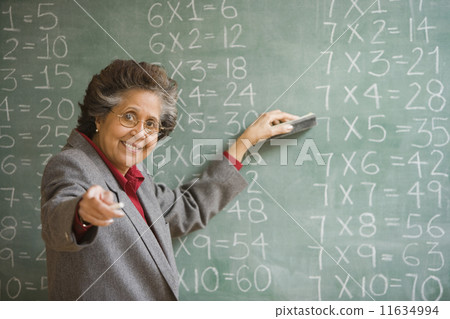 Senior Hispanic female teacher in front of blackboard Senior Hispanic female teacher in front of blackboard 11634994