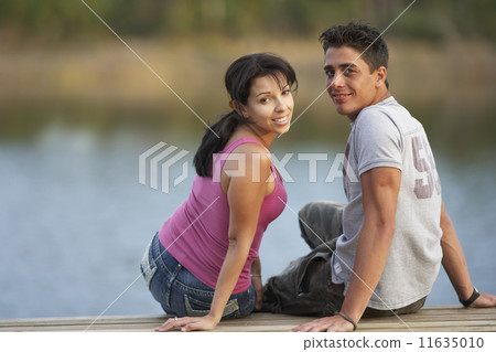 Multi-ethnic couple sitting on dock Multi-ethnic couple sitting on dock 11635010