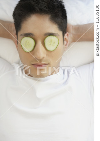 Asian man with cucumber slices on eyes Asian man with cucumber slices on eyes 11635130