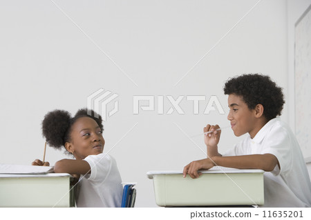 Hispanic boy blowing spitball on girl in class 11635201